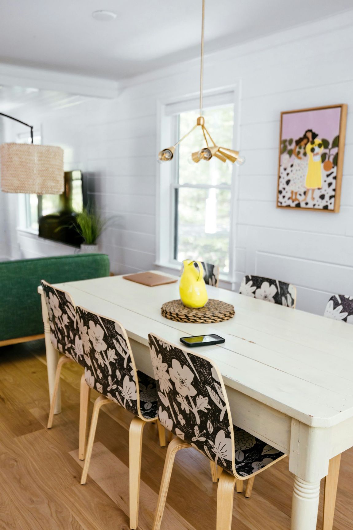 Dining room with white table, floral-patterned chairs, and a whimsical light fixture; artwork on wall.