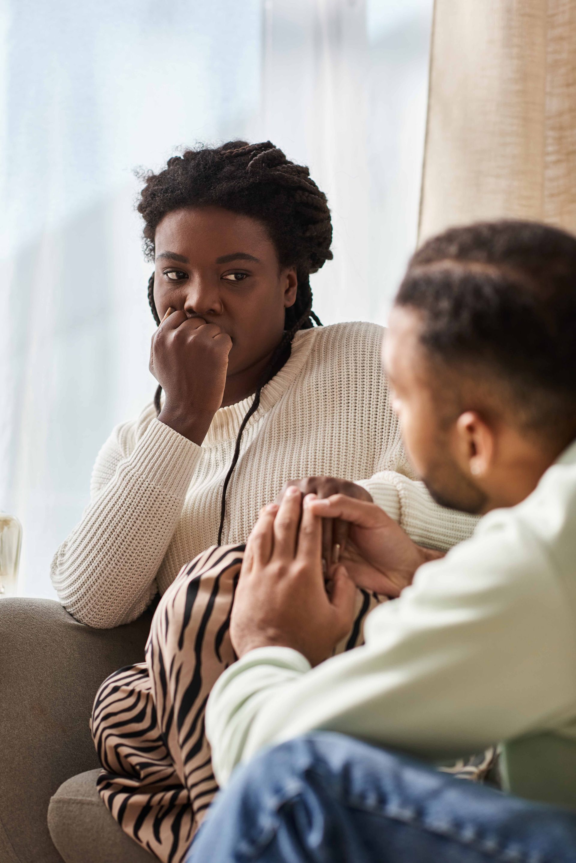Couple in therapy: woman covers ears, distressed; man gestures, therapist listens. Indoor, neutral tones.