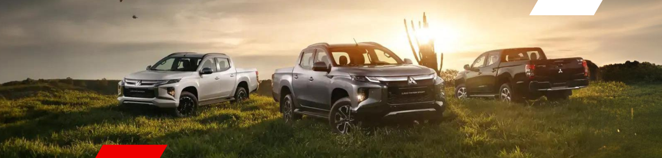 Diversas caminhonetes estacionadas em um campo gramado com o pôr do sol ao fundo.