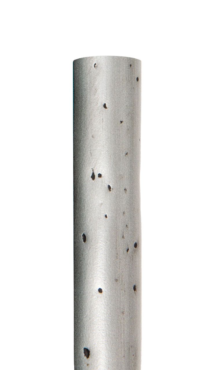 A close up of a metal pipe with black spots on it on a white background.