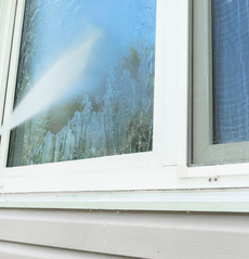 Person spraying water on a white window, cleaning the glass and frame.