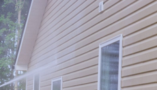 Side of a beige house with white-trimmed windows and a sloped roof, viewed through rain or mist.