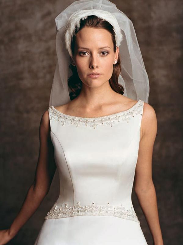 Woman in a white wedding dress and veil, standing against a dark studio backdrop.