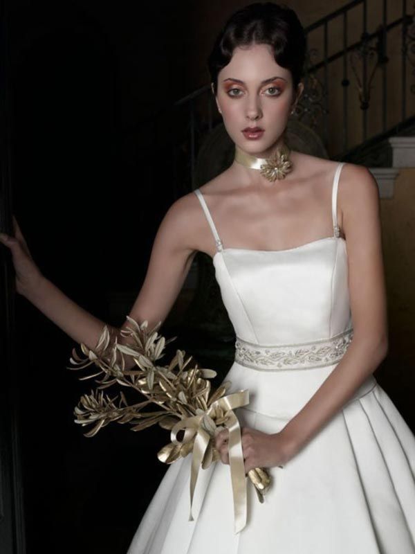 Woman in a white dress holding a gold floral bouquet on a staircase.