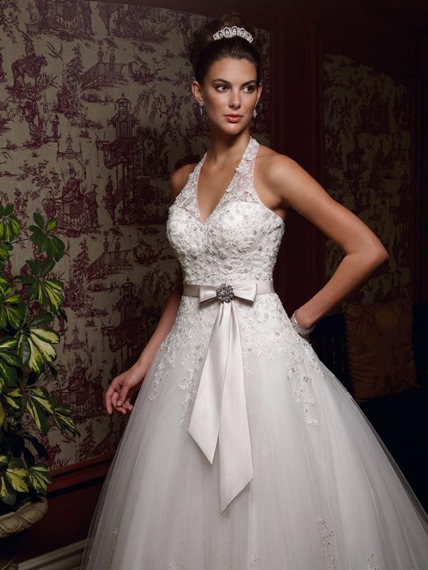 Woman in white beaded bridal gown with tulle skirt and silver sash, posing indoors against patterned wallpaper