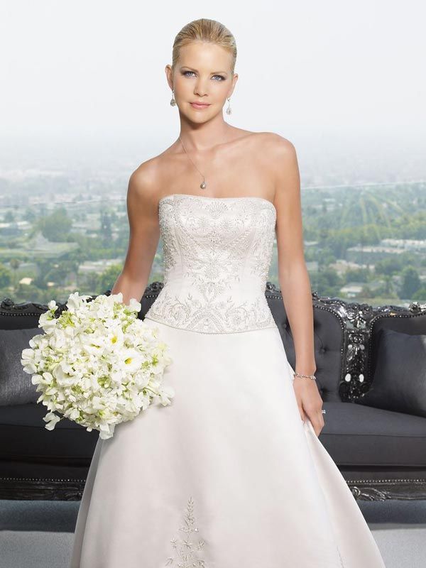 Bridal portrait of a woman in a strapless white gown holding a white bouquet with city view behind her