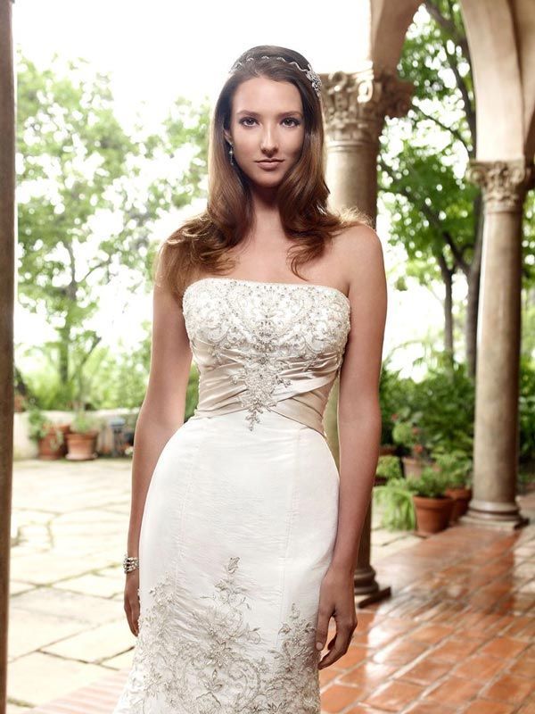 Woman in a strapless white lace dress standing on a tiled patio with greenery and columns in the background