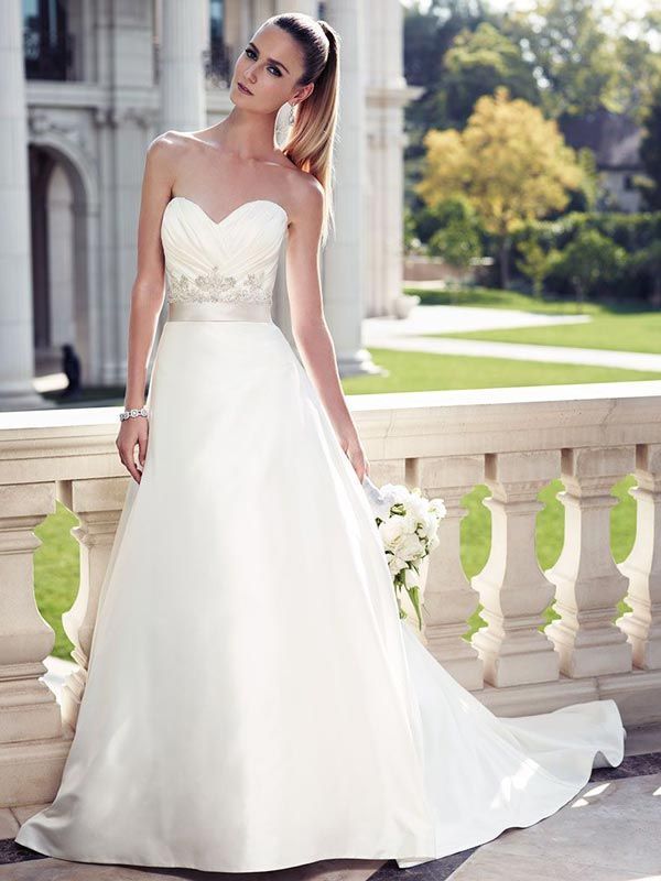 Woman in a white strapless wedding dress standing on a sunlit balcony garden.