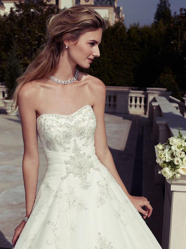 Bride in a white strapless gown holding a bouquet on a sunny terrace