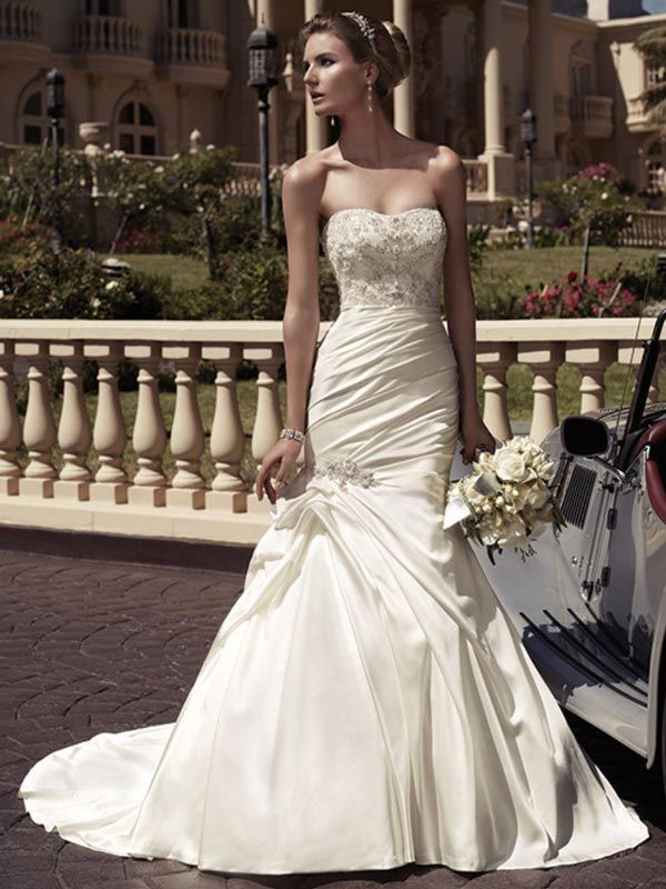 Bride in a strapless white wedding gown standing outdoors beside a luxury car and bouquet