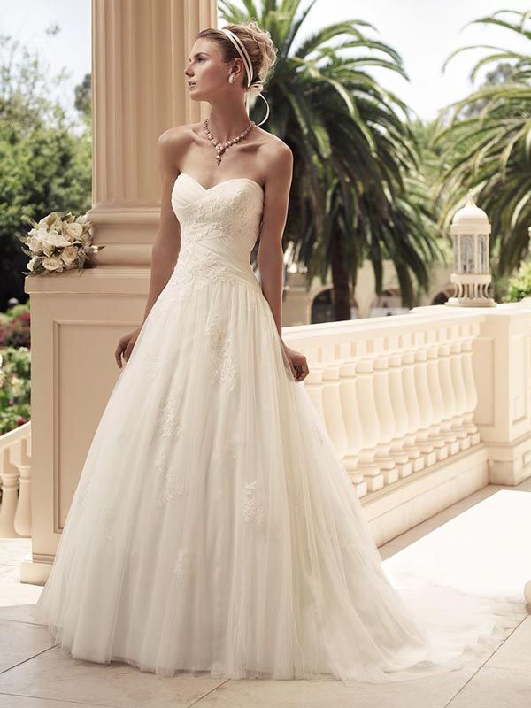 Woman in a strapless ivory wedding gown standing on a sunlit terrace with palm trees in the background
