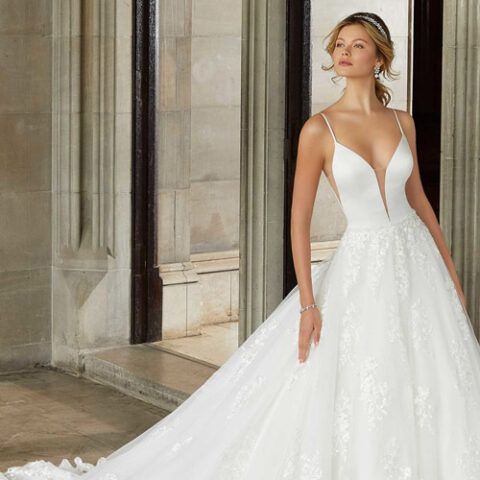 Woman in a white wedding gown standing in a stone archway, with a long train trailing behind her.
