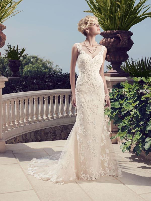 Woman in a white lace gown standing on a terrace with palm plants and a stone balustrade.