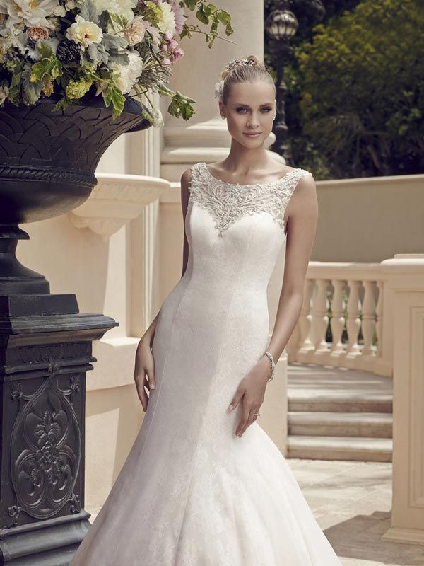 Woman in a white beaded gown posing beside a stone balcony and floral arrangement.