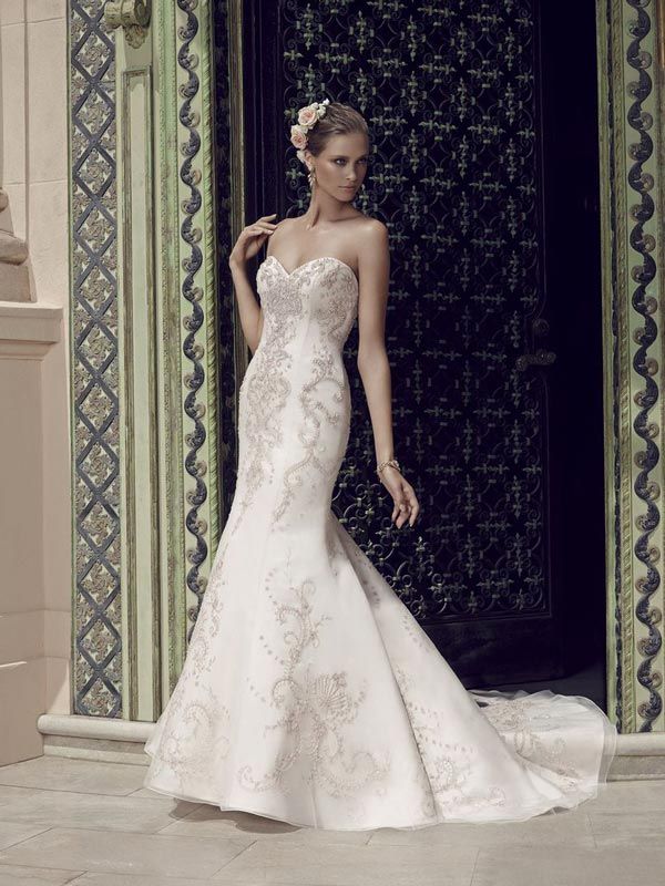 Woman in a white strapless gown posing by an ornate doorway.