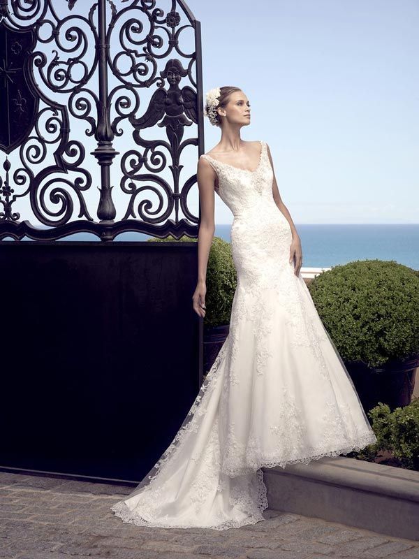 Bride in a white lace gown leaning beside an ornate gate with ocean view beyond.