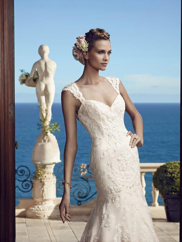 Bride in a white lace gown standing on a seaside terrace with a statue and ocean view behind her