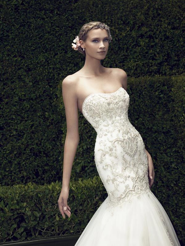 Woman in a white strapless lace wedding dress standing against a dark green hedge.