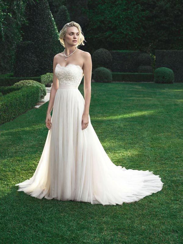 Woman in a white strapless gown standing on a manicured lawn in a garden.