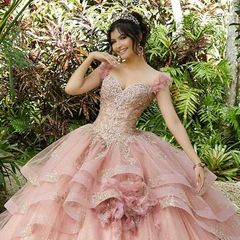 Woman in a pink layered gown posing in a garden with lush greenery.