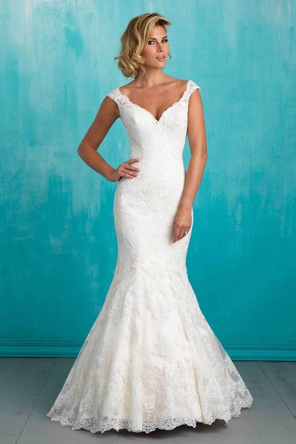 Woman in a white lace mermaid wedding dress posing against a turquoise wall