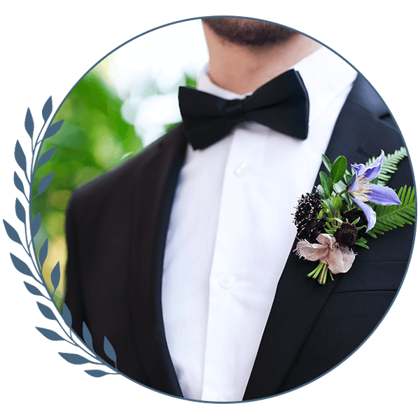 Man in a black tuxedo with a bow tie and boutonniere, framed in a circular portrait with leafy border
