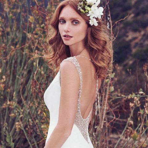 Woman in a white dress with floral hairpiece, standing outdoors against a natural background.