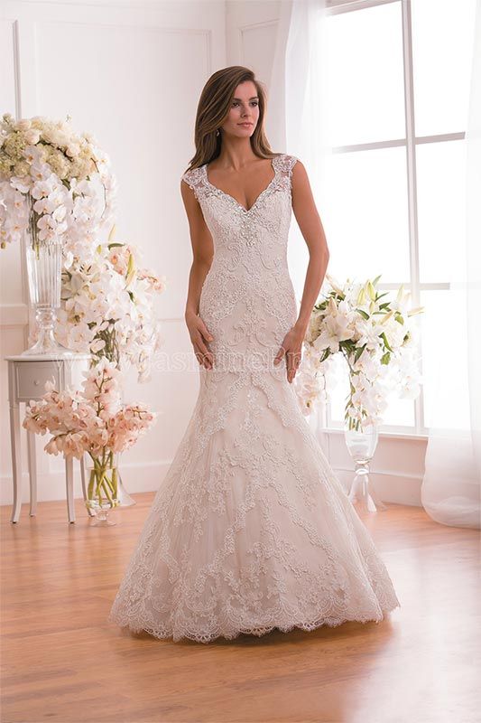 Woman in a beaded white wedding dress standing in a bright room with floral arrangements.