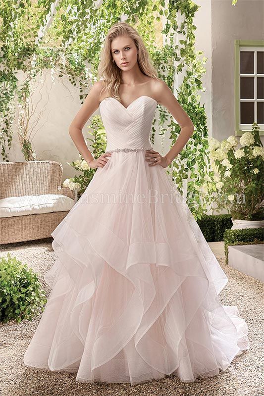 Woman in a blush pink strapless gown standing in a garden courtyard.