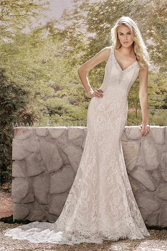 Woman in a white lace gown standing outdoors beside a stone wall and trees