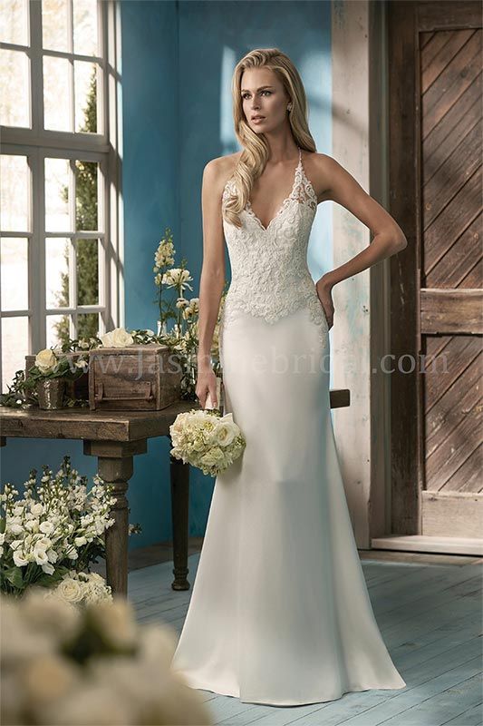 Bride in a lace white wedding gown holding a bouquet by a sunlit window and wooden door