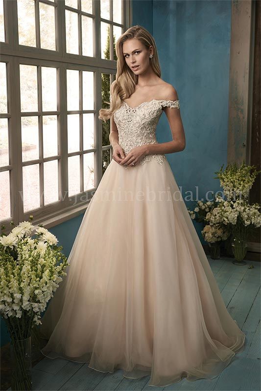 Woman in a blush ball gown standing by a window in a softly lit room