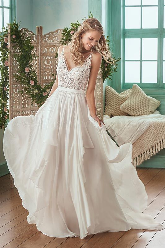 Woman in a white lace wedding dress standing in a bright room, holding her skirt.