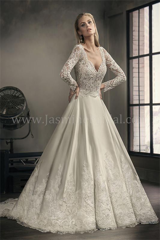 Bride in a long-sleeved lace wedding gown standing by a window in a moody studio setting
