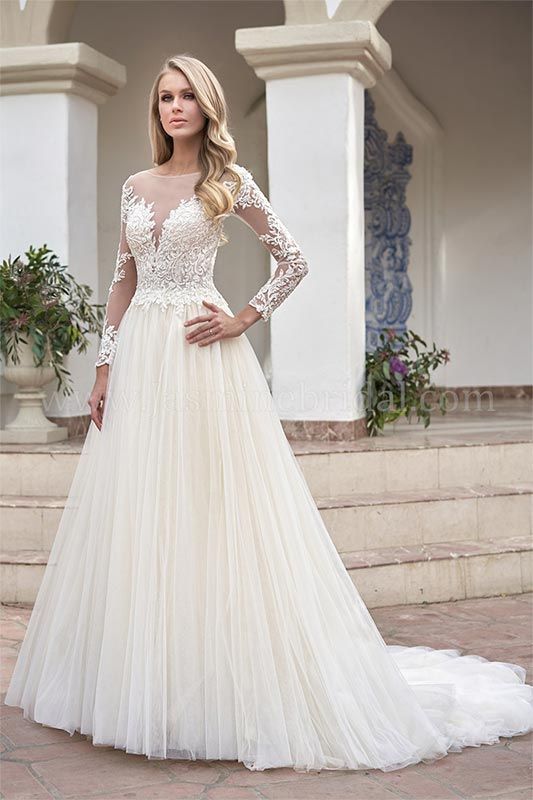 Woman in a white lace long-sleeve bridal gown with a full tulle skirt, standing on stone steps by columns