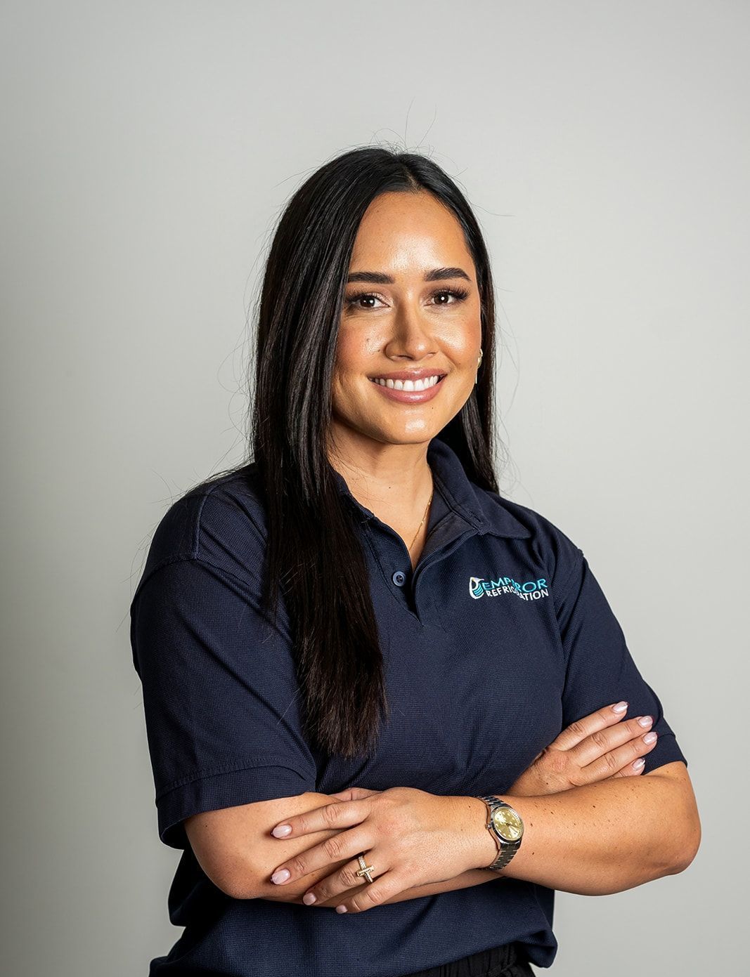 Woman with dark hair smiles, arms crossed, wearing a dark blue polo shirt with a logo.