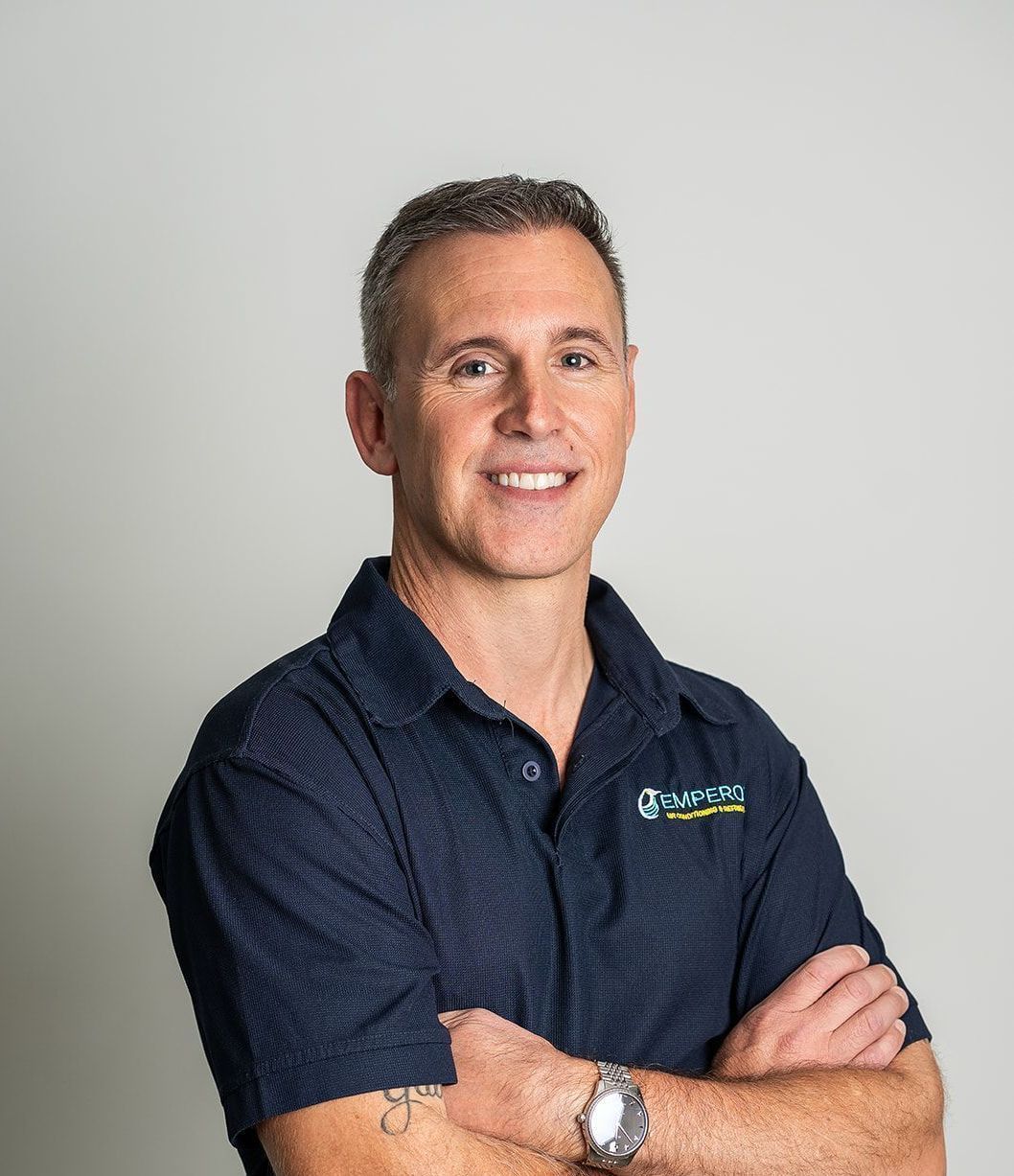 Man with crossed arms, wearing a navy blue collared shirt, smiles at the camera.