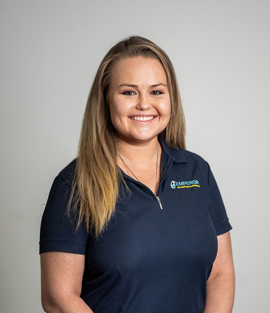 Woman in a dark blue polo shirt, smiling, with light brown hair. White background.