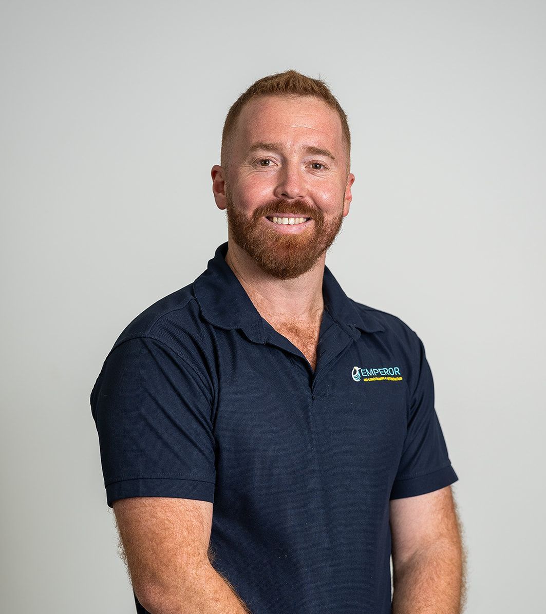 Man with red hair and beard smiles, wearing a blue polo shirt, against a white background.