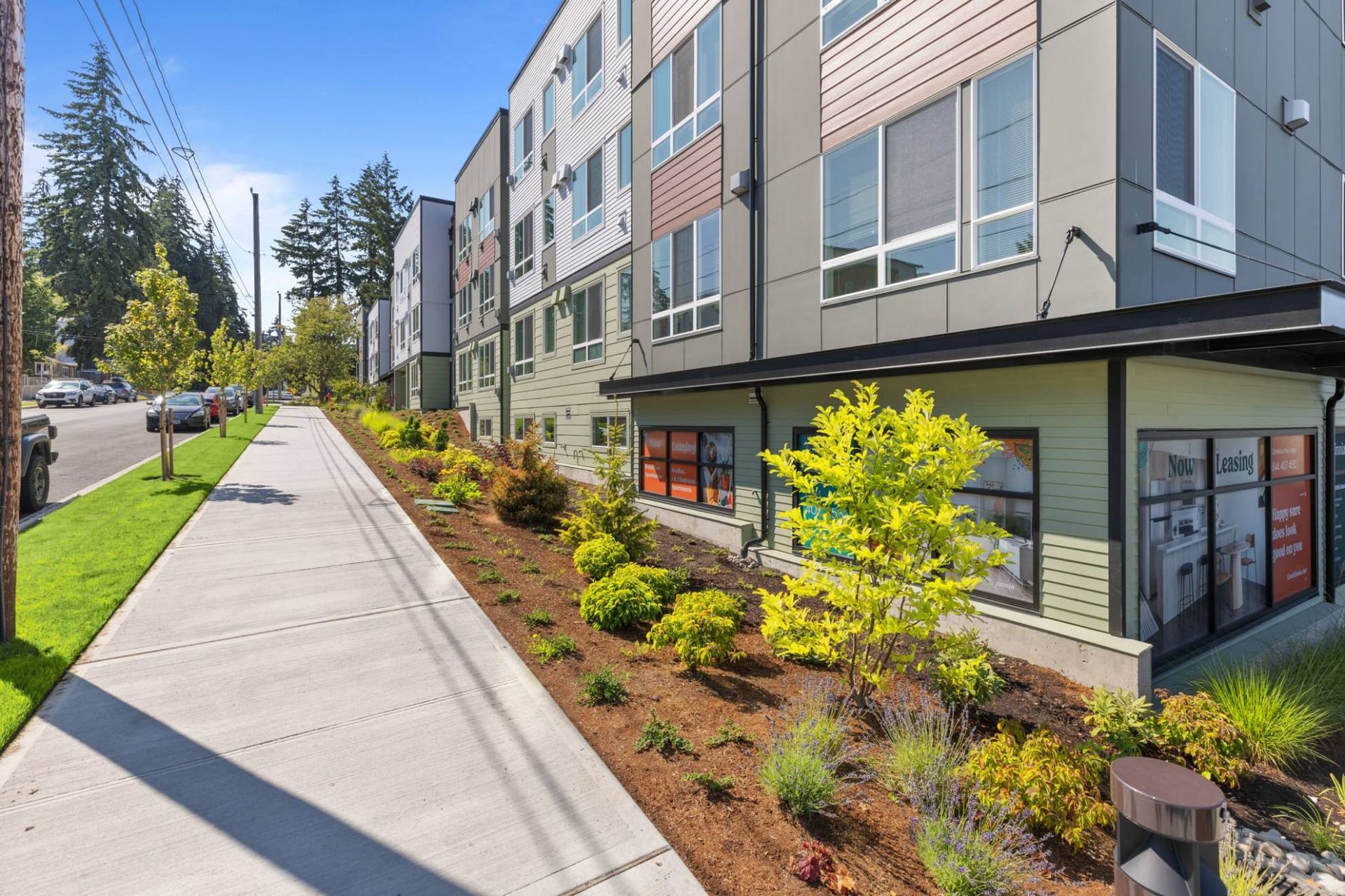 Exterior view of a modern apartment building with a sidewalk, landscaping, and leasing signage at Zinnia Apartments in Shoreline, WA.