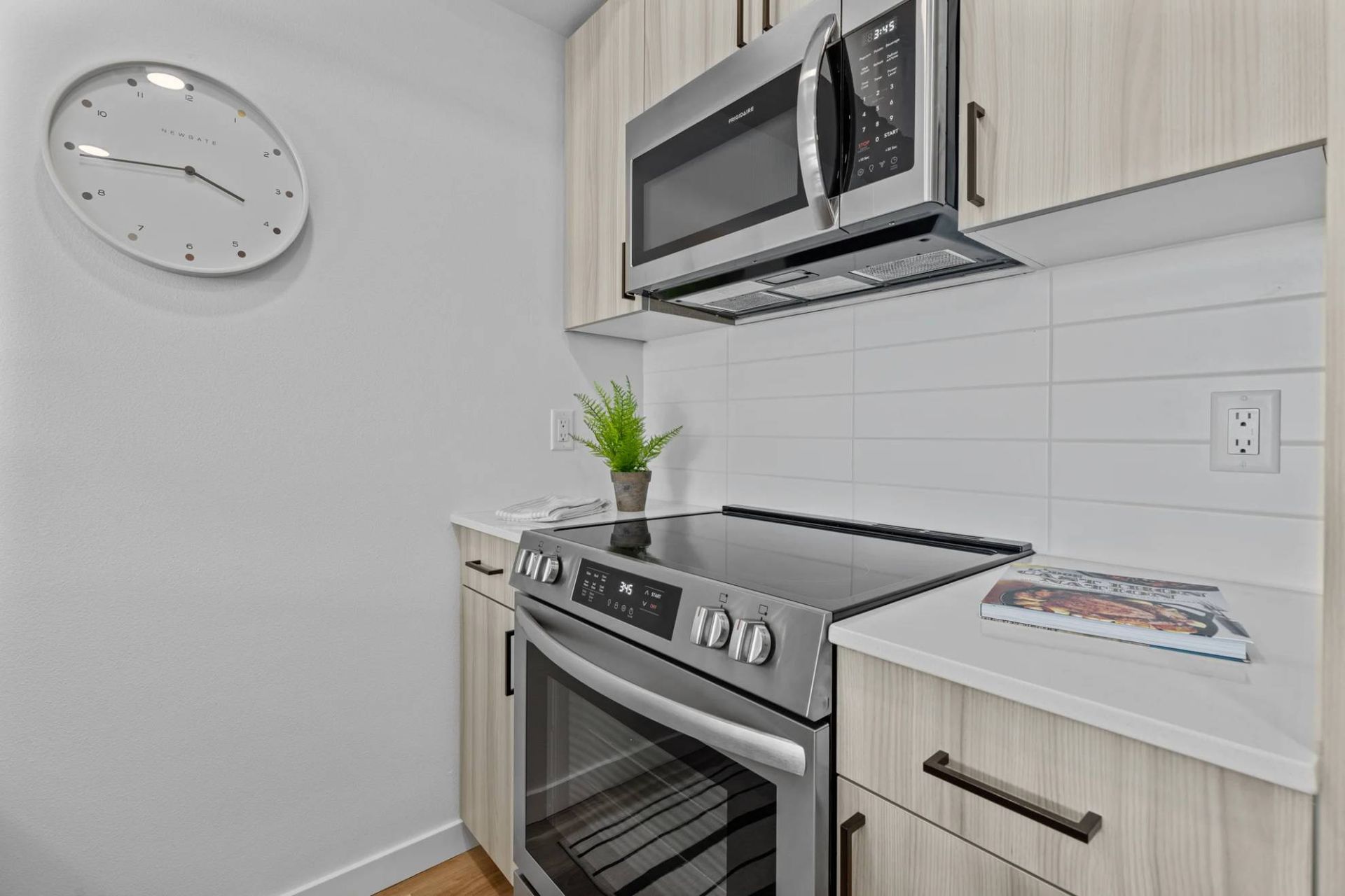 Kitchen with stainless steel stove and microwave, white tile backsplash, and light wood cabinets at Zinnia Apartments in Shoreline, WA.
