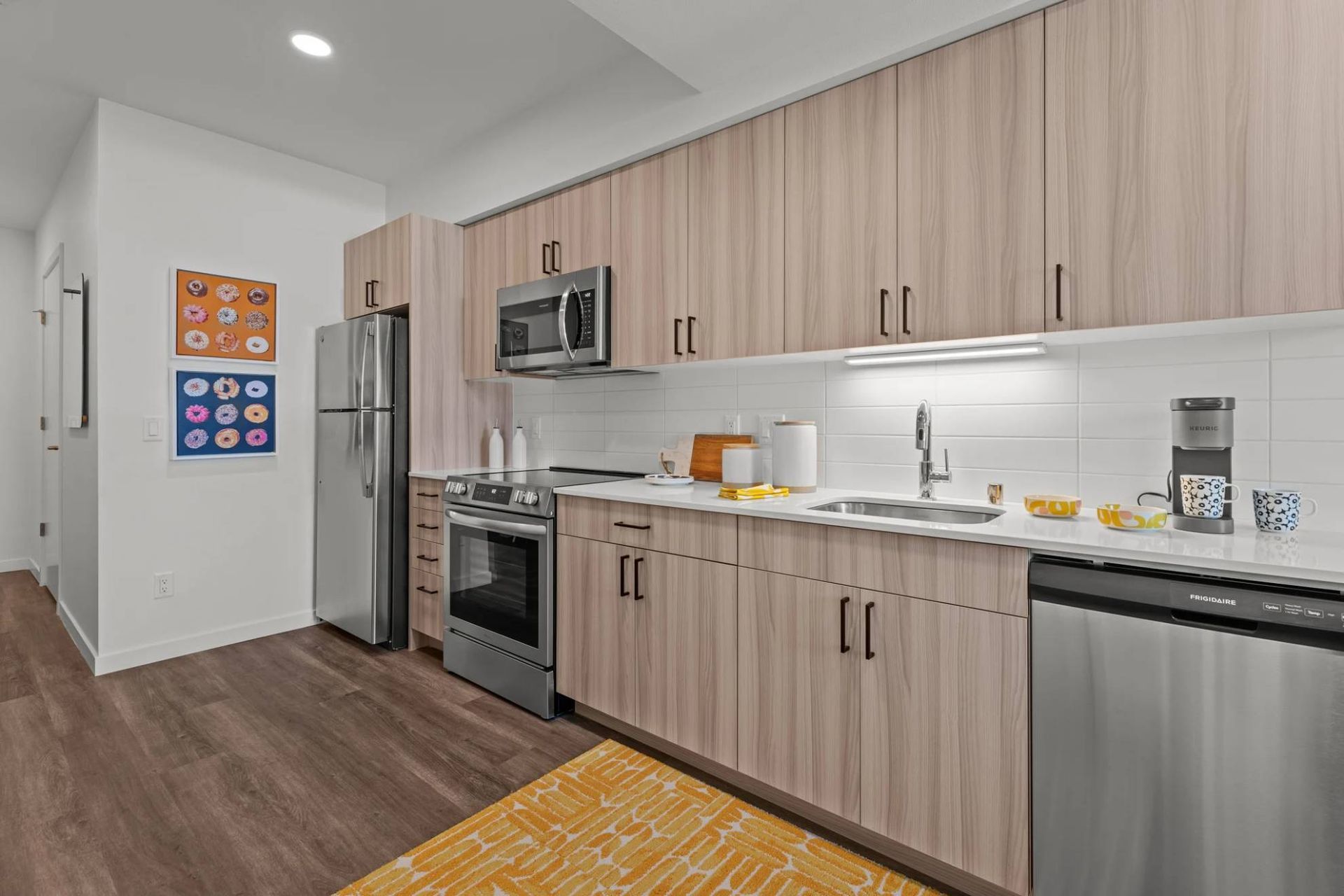 Modern apartment kitchen with light wood cabinets, stainless steel appliances, and a white tile backsplash at Zinnia Apartments in Shoreline, WA.