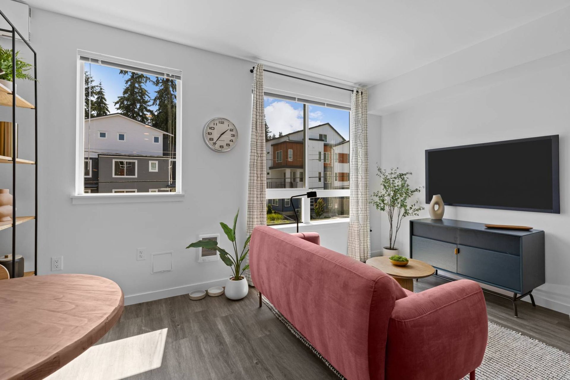 Bright living room in an apartment with a pink sofa, large windows, and a wall-mounted TV at Zinnia Apartments in Shoreline, WA.