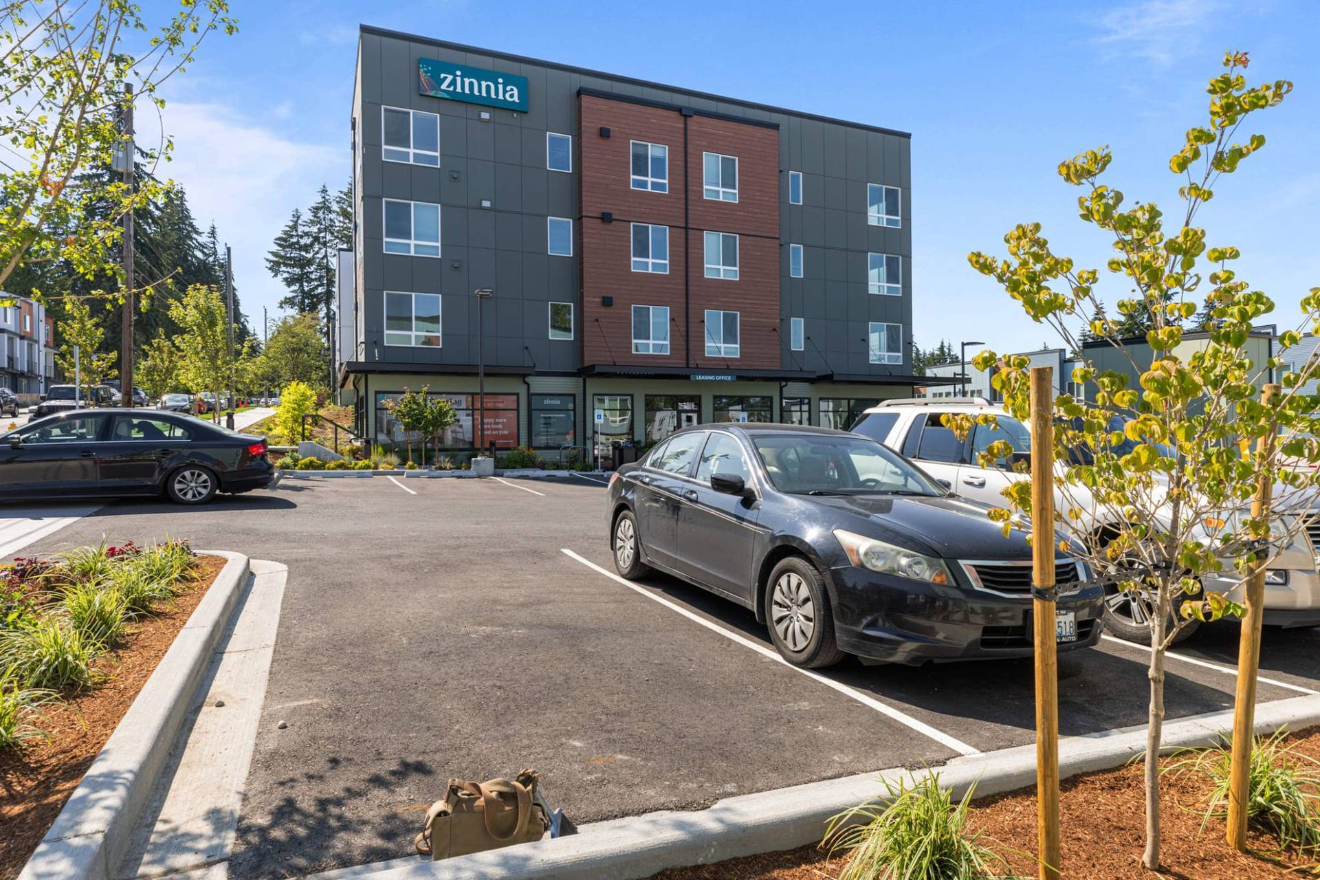 Exterior view of a modern apartment building with a parking lot and landscaped surroundings at Zinnia Apartments in Shoreline, WA.