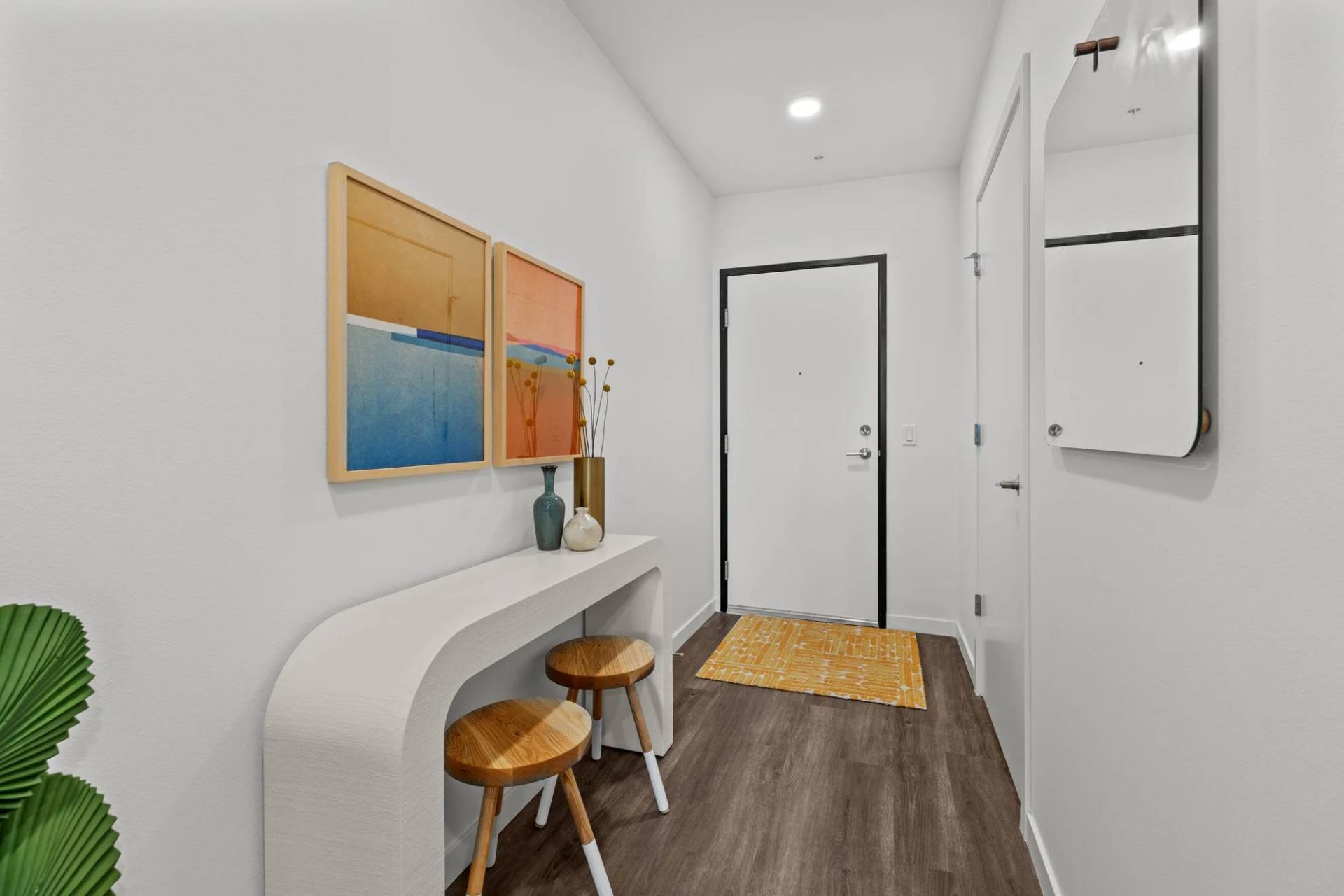 Entry hallway of an apartment featuring a curved white console, two stools, wall art, and a mirror at Zinnia Apartments in Shoreline, WA.