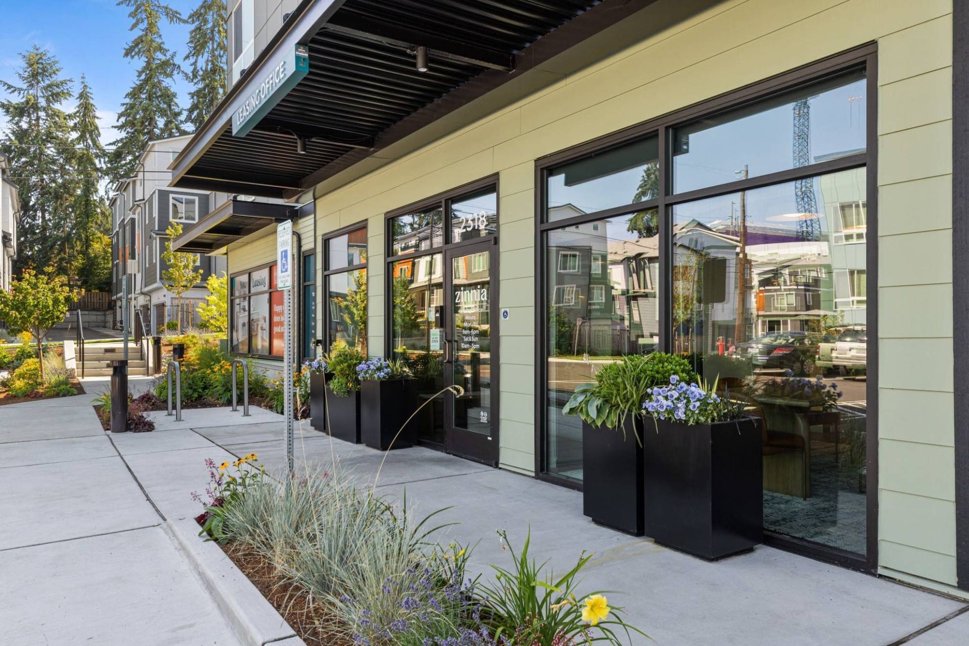 Exterior view of the leasing office with large glass doors and planters along the entrance at Zinnia Apartments in Shoreline, WA.