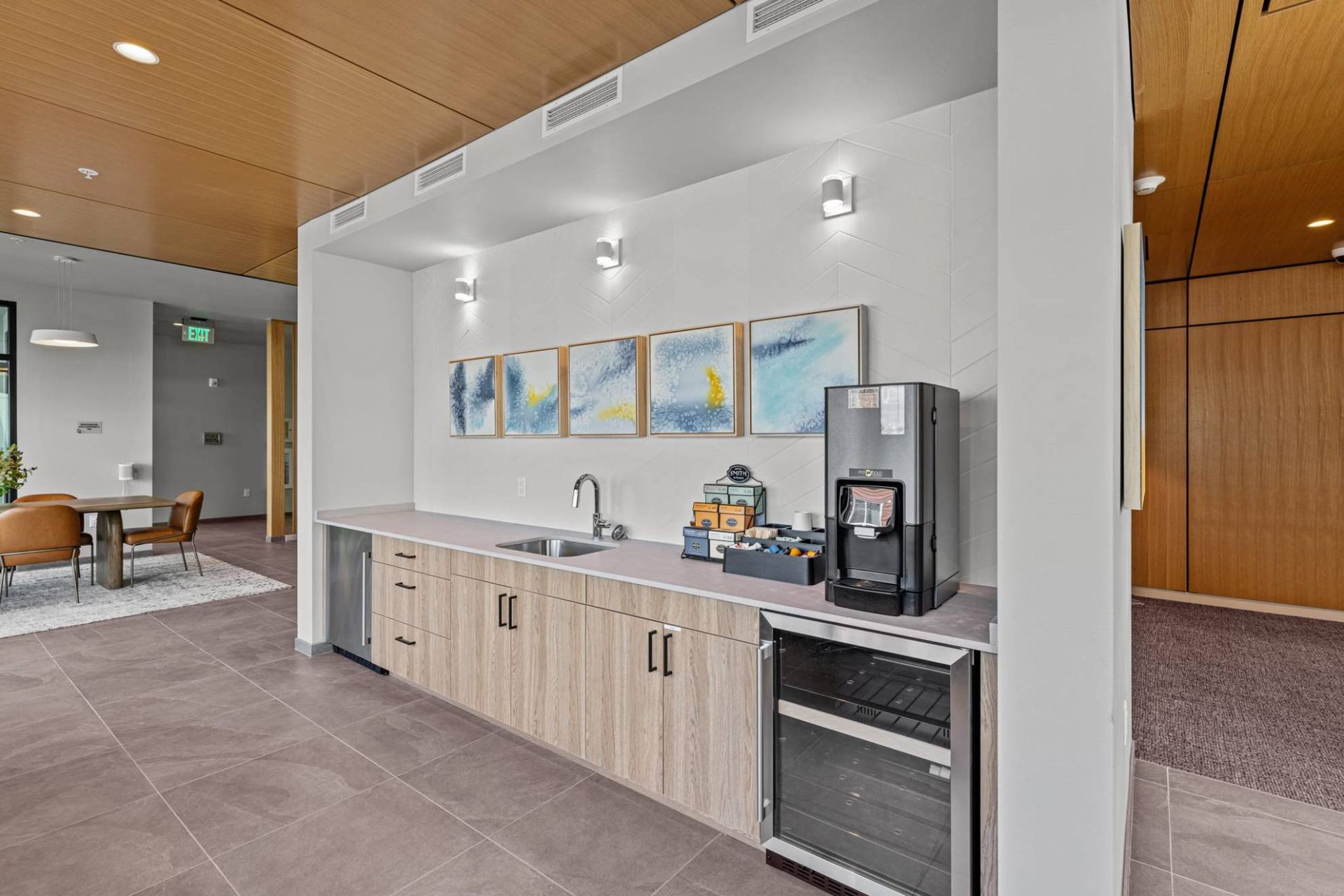 Communal kitchenette with sink, coffee machine, mini-fridge, and wall art at Zinnia Apartments in Shoreline, WA.