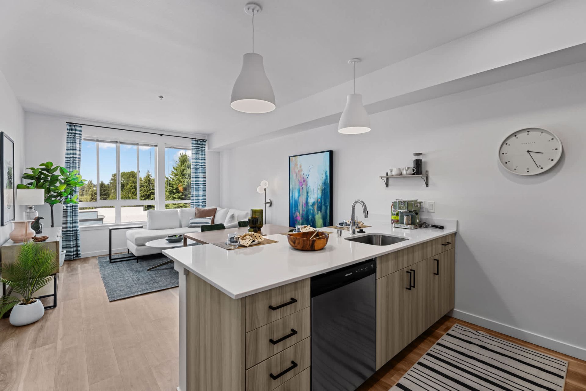 Open-concept kitchen with island and living area, large window providing natural light at Zinnia Apartments in Shoreline, WA.