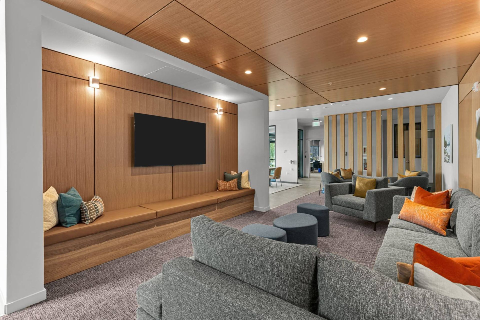 Modern community lounge with wood-paneled wall, mounted TV, and sectional seating at Zinnia Apartments in Shoreline, WA.