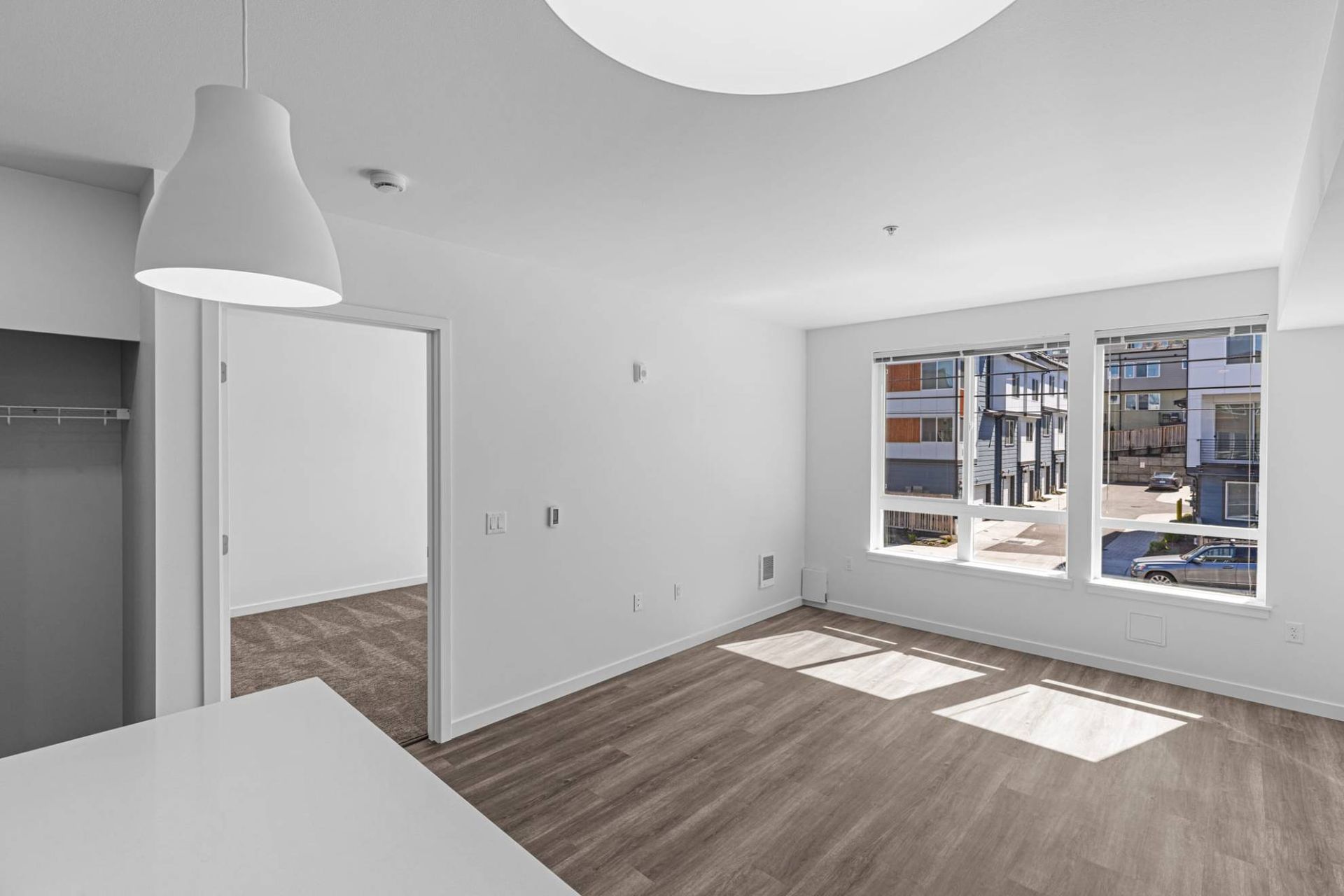 Bright empty living area with white walls, wood-style flooring, and large front windows at Zinnia Apartments in Shoreline, WA.